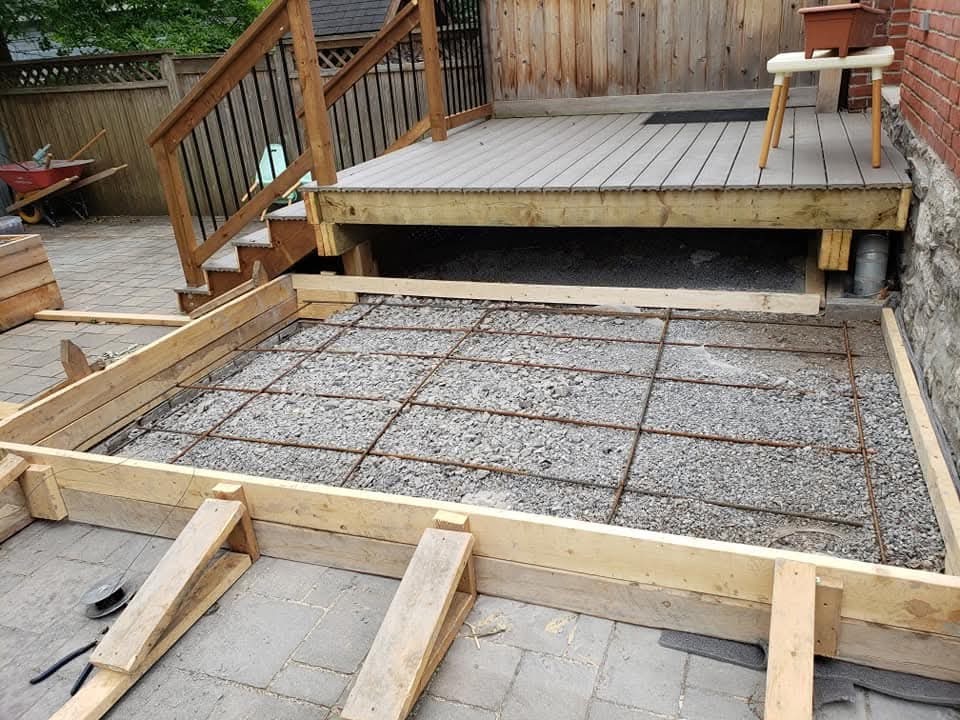 Timber forms and a grid of reinforcement over a gravel base beside a wooden deck