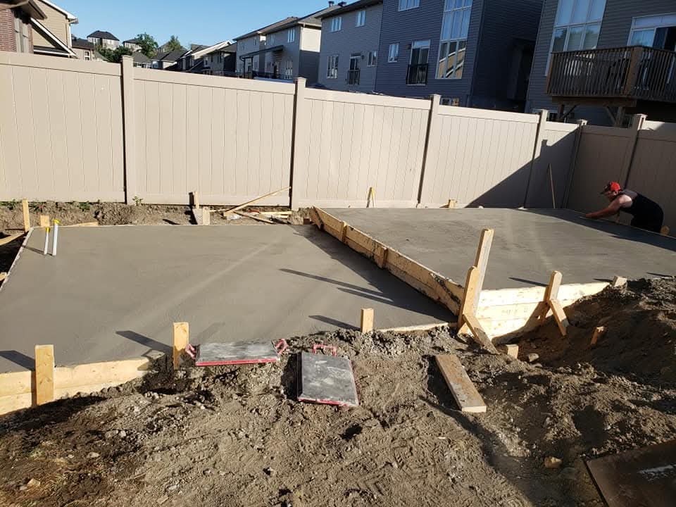 Fresh concrete patio beside a beige vinyl fence with formwork and equipment visible