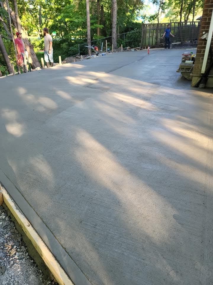 Large concrete patio extending along a house toward a wooded backyard
