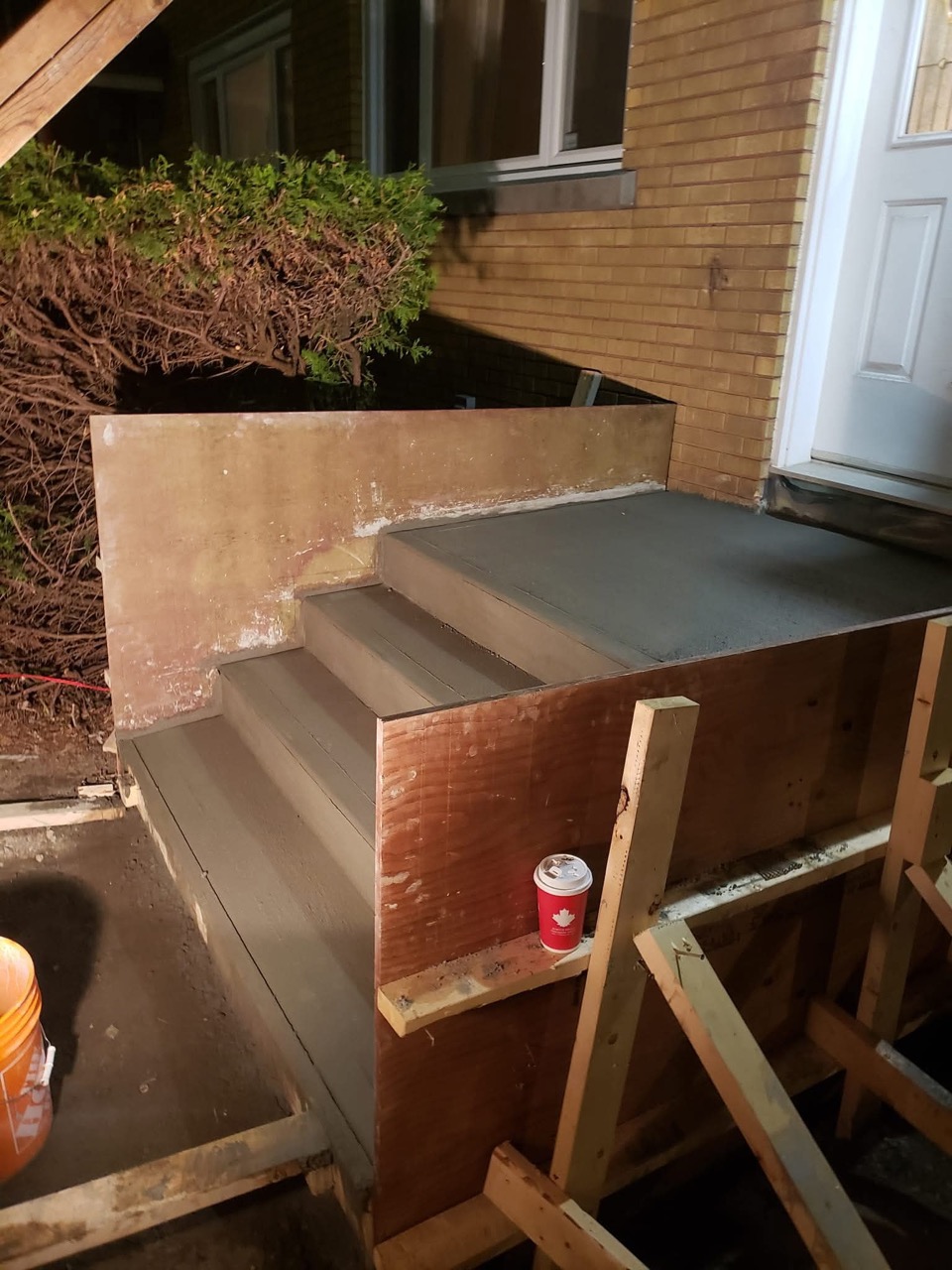 New concrete front steps beside a brick house with wooden formwork still attached