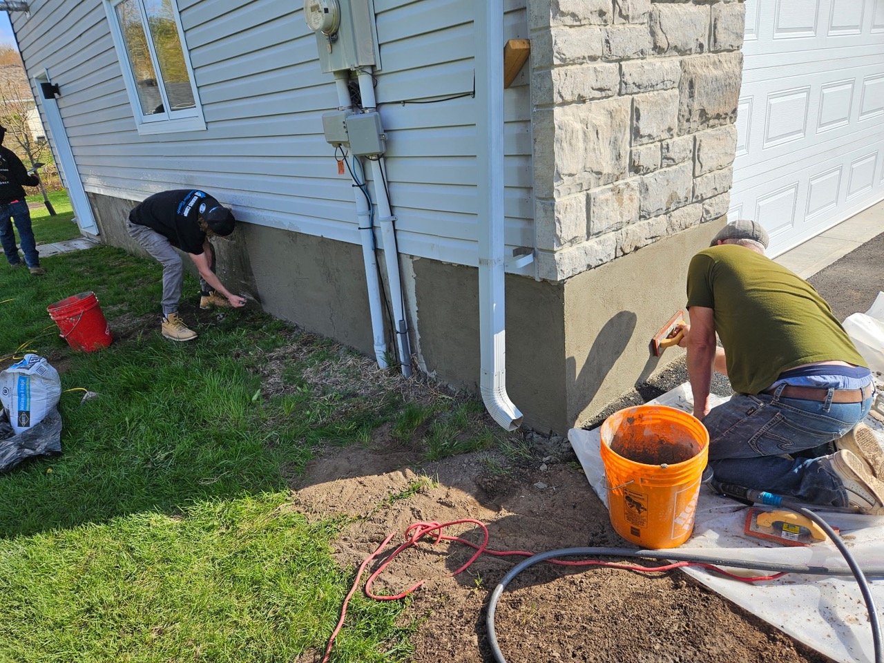 Crew members applying parging to a foundation beneath siding and stone cladding