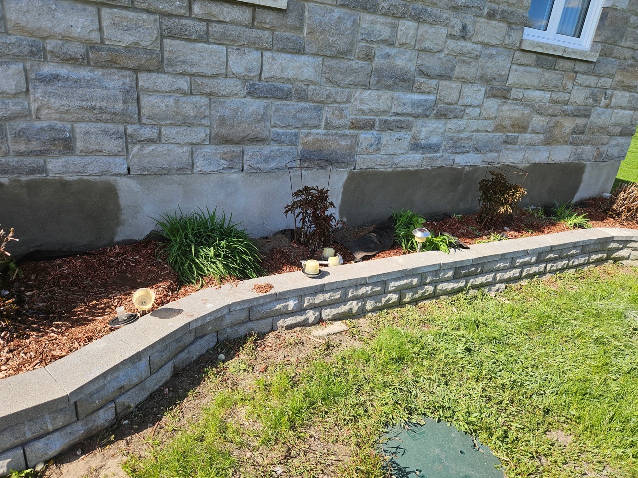 Grey parging along the base of a stone-clad wall behind a planted garden bed