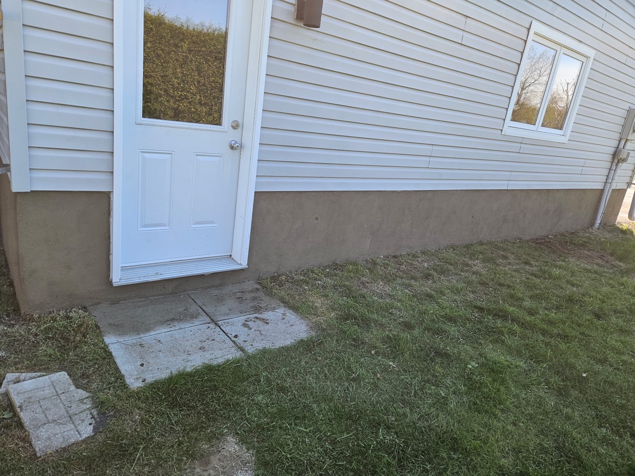 Continuous grey foundation finish beside a white side door and lawn