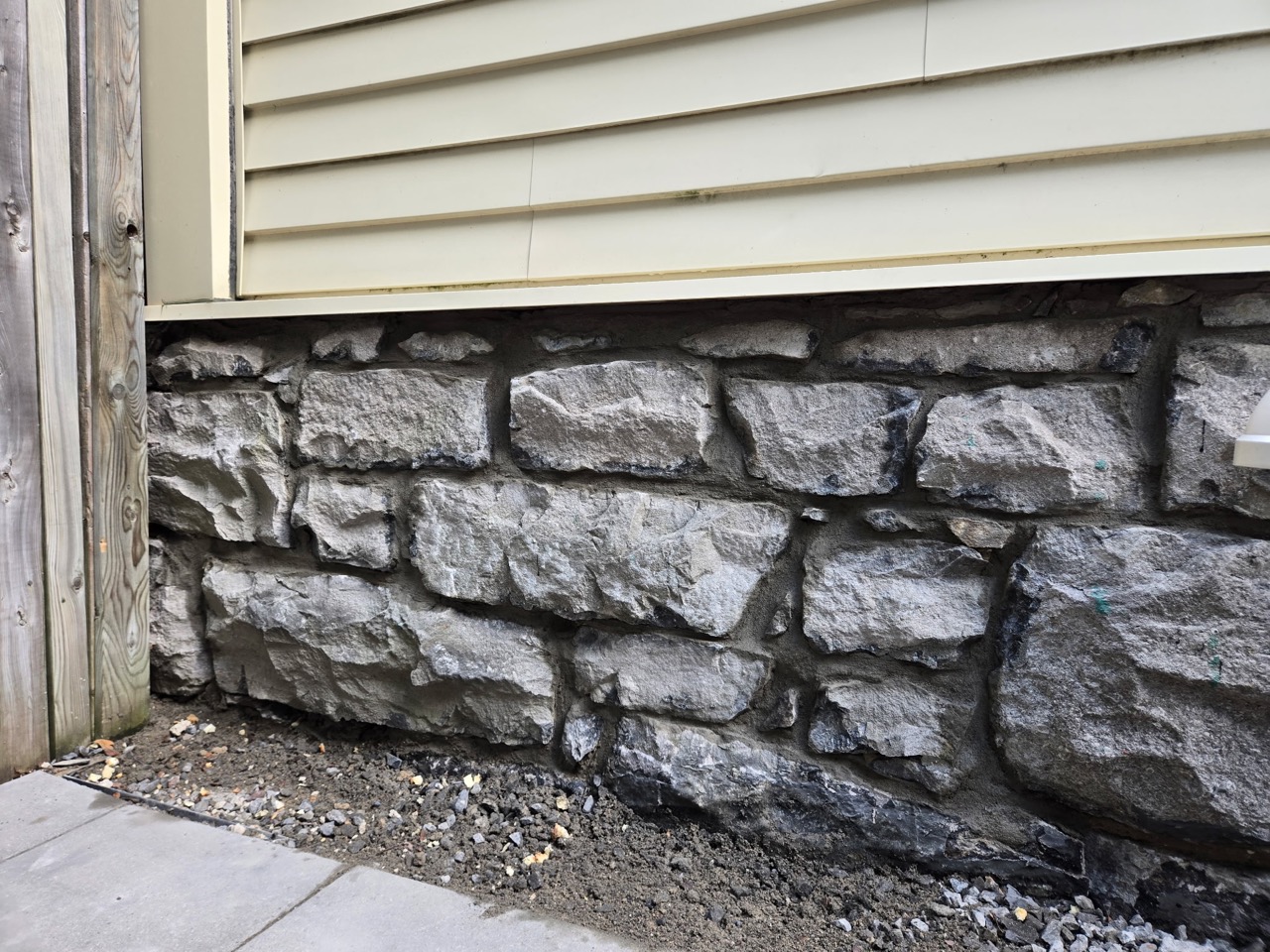 Exposed stone foundation with repaired mortar joints beneath light-coloured siding